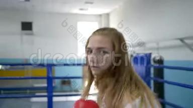 拳击场上的女运动员戴着拳击手套准确地挥拳，并在训练时看着摄像机